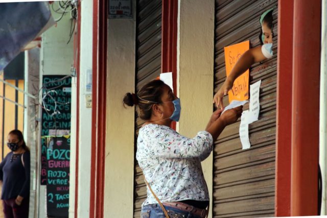 Una mujer compra en una farmacia, una trabajadora la atiende detrás de la cortina del negocio.